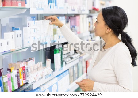 Beautiful mature Asian woman choosing cosmetics at the drugstore reaching for something on a shelf copyspace pharmacy buyer shopping shop store consumer customer purchase beauty lifestyle