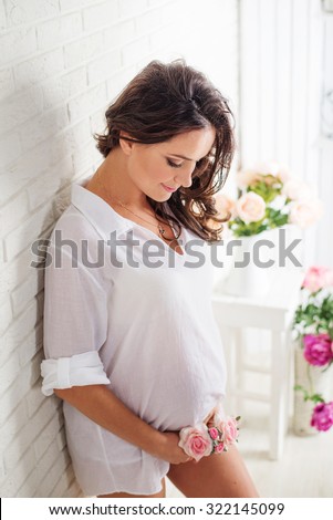 Pregnant Happy smiling Woman standing near the wall and caressing her belly. Mom Expecting Baby. Pregnant Woman Belly. Pregnancy. Beautiful Pregnant Woman.  Maternity concept. Baby Shower