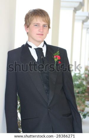 Young man in formal wear leaning against a wall.