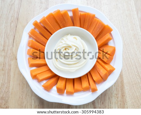 carrot sticks with mayonnaise on white plate placed on a wooden background.