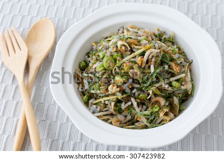 Thai cuisine , Thai Southern food, Spicy blue rice salad with mix vegetable on white plate, placed on a gray tablecloth background.