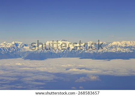 View through aircraft window at Himalayan mountains. Above the clouds