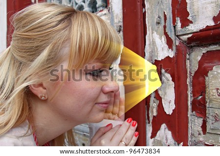 Young woman spying through a keyhole. There is golden light behind the old door