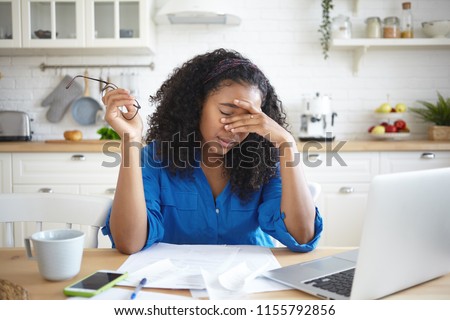 Tired young African American single mother feeling stressed because of financial problems, working through finances in kitchen late at night, doesn\'t have enough money to pay off mortage debt