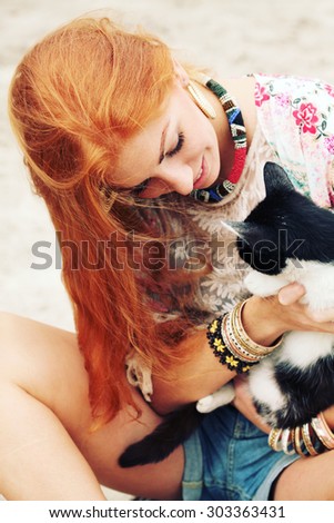 Young happy smiling red-haired girl dressed in hippie bohemian style hugging cat outdoors. Embracing, love, lifestyle.