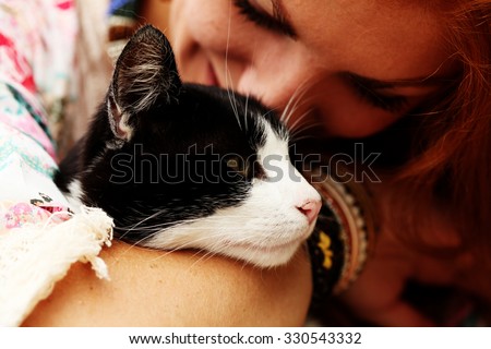 Young happy smiling red-haired girl dressed in hippie bohemian style hugging cat outdoors. Embracing, love, lifestyle.