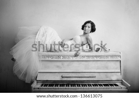 Beautiful woman in luxurious dress lying on the piano. Retro style