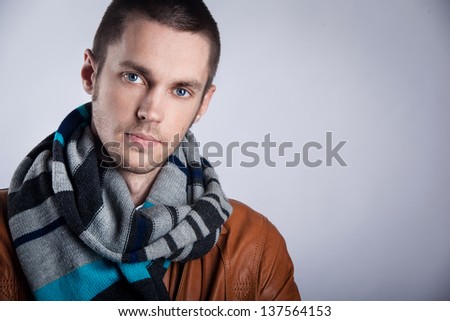 Portrait of  young man in brown jacket with striped scarf over gray background. Close-up. studio shot