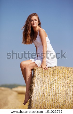 young woman sitting in a field on a haystack