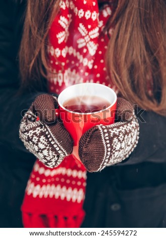 cup of hot tea, women\'s hands in mittens on a background of a Christmas scarf, close-up