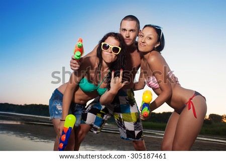 Group of young joyful young people playing and posing with water pistols on the beach