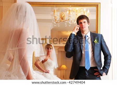 The groom and the bride against a mirror. The groom speaks by phone.