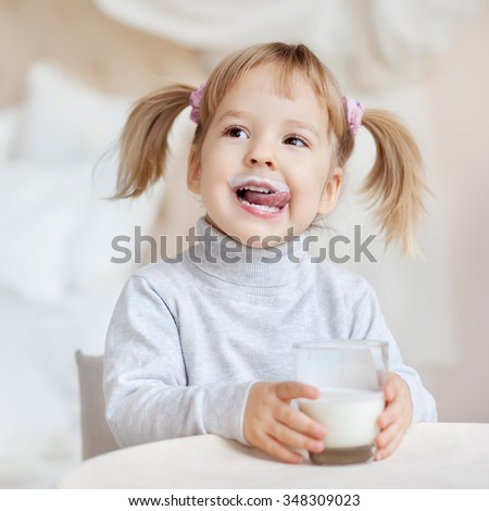 Cute little girl with milk mustache holding glass of milk
