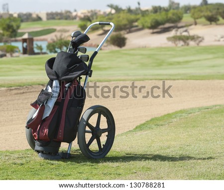 Golf caddy trolley and bag on a golf course with bunker in the background