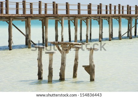 Long wooden jetty on a tropical island stretching out into the sea with stools and table