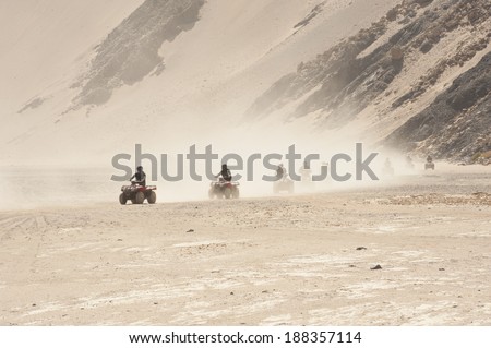 Group of quad bikes doing desert safari through an arid barren landscape with dust cloud
