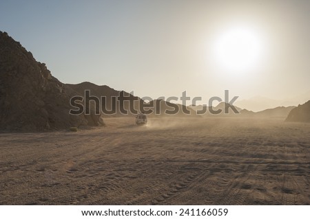 Off road vehicle on safari traveling through arid desolate desert landscape with sunset