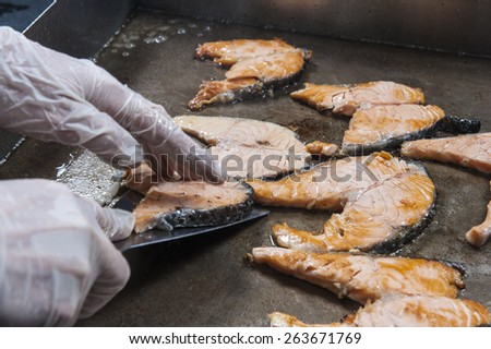 Salmon steaks with chefs hands cooking on grill hot plate at a hotel restaurant buffet