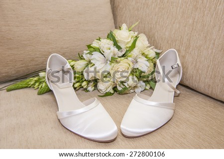Pair of womens brides wedding shoes on a sofa with bouquet bunch of flowers