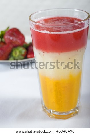 Fruit cocktail drink with three layers & strawberries in background