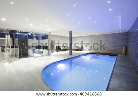 Relaxing indoor swimming pool with lighting and a corner for rest. Luxury resort swimming pool with beautiful clean blue water and  light effects around the swimming pool.