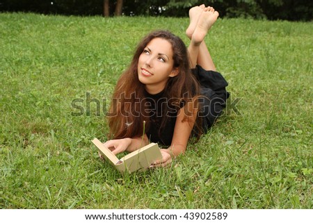 The beautiful young girl in park on lawn reads the book