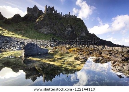 The famous Dunluce Castle - a UNESCO landmark from the Causeway Coast of Northern Ireland - reflected in a tidal pool from beneath the cliffs.