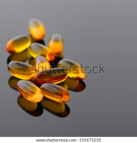 Close-up of fish oil capsules on gray glossy background.