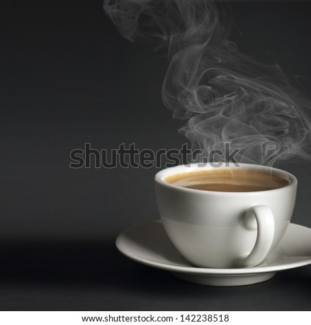White cup of hot coffee with steam on dark gray background.
