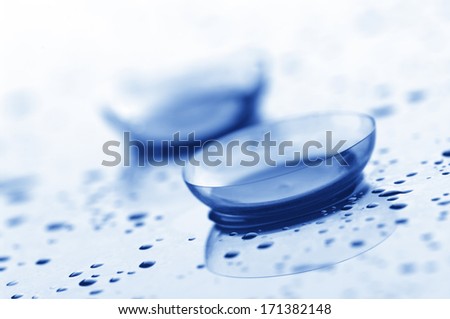 Close-up of two contact lenses with drops on light background. Blue toned image.