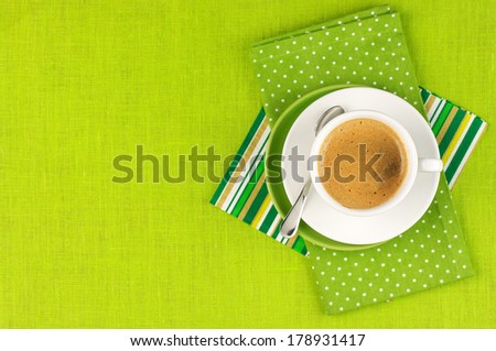White cup of coffee on green linen. Top view.