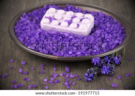 Violet bath salt and soap in dish on wooden background.