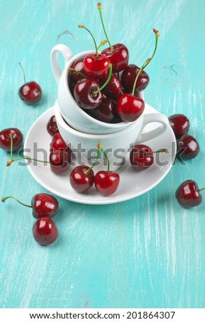 Cherries in cup on turquoise wooden background.