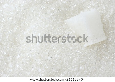 Granulated sugar and sugar cube as background.
