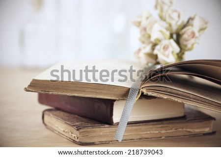 Stack of books and roses on wooden table. Shallow DOF.