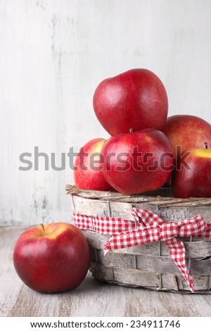 Red apples in basket on rustic painted wooden background.