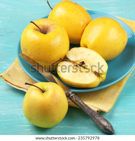 Yellow Golden Delicious apples in plate with linen napkin on turquoise rustic wooden table.
