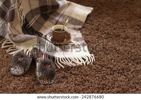Woolen checked plaid, slippers and coffee cup on shaggy carpet. Focus on slippers.