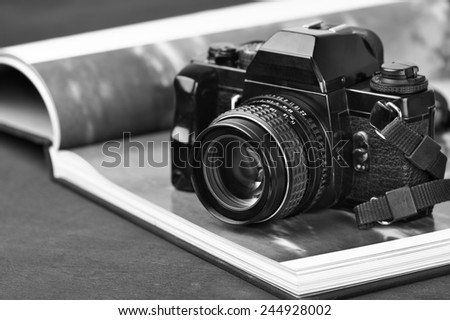 Vintage mechanical 35mm film photo camera SLR and photo book with monochrome picture. Black and white image.