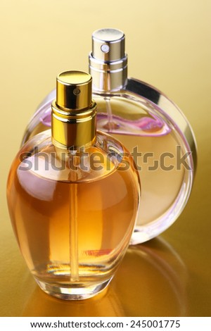 Two bottles of woman perfume on gold background.