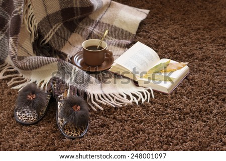 Woolen plaid, coffee cup, book and slippers on shaggy carpet. Focus on slippers.
