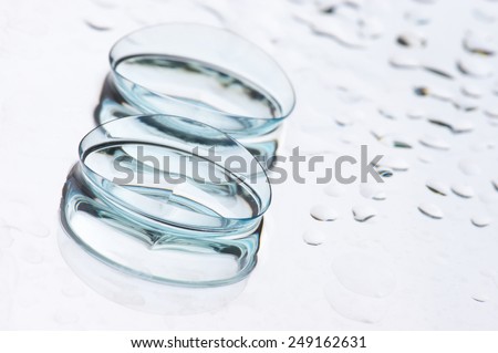 Close-up of two wet soft contact lenses with reflection on light background with drops and copy space. Shallow DOF.