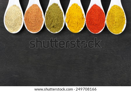 Assorted powder spices in white spoons on black wood. Top view point.