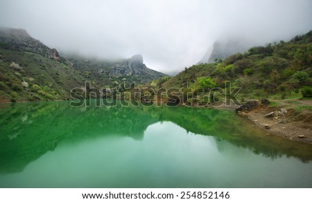 Tranquil mountain lake with green water and reflection at overcast weather with fog. Arpat, Crimea.
