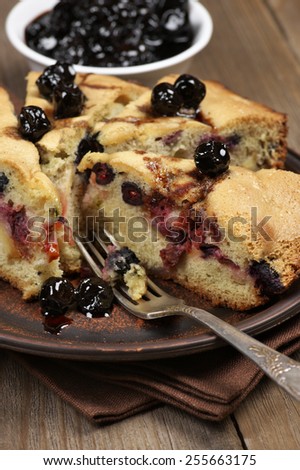 Slices of fruit pie with berries in brown plate on wooden table.