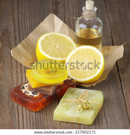 Various natural soaps, lemon and bottle of oil on rustic wooden background.