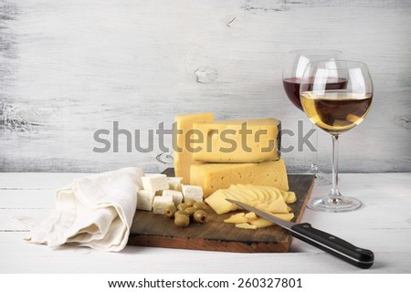 Assorted cheese with olives on board and glasses of red and white wine on rustic wooden background.