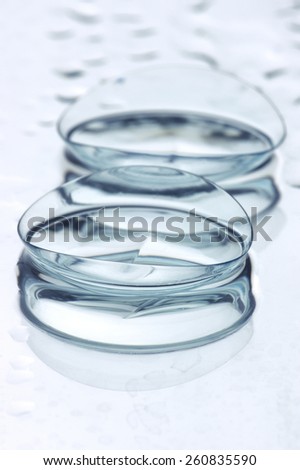 Extreme close-up of two wet soft contact lenses with reflection on light background with drops. Shallow DOF, focus on foreground.