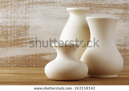 Three empty white unglazed ceramic vases on wooden table against rustic wooden wall. Toned image. Shallow DOF, focus on middle vase.