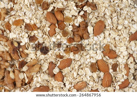 Pile of dry oatmeal flakes with walnuts, almonds and raisins as background. Top view point.